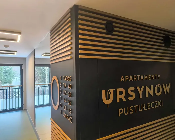 Napis Apartamenty Ursynów Pustułeczki i wykaz pięter na ścianie z poziomymi lamelami