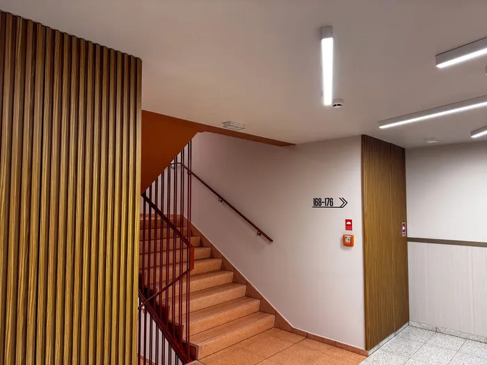 Lamele przy klatce schodowej i drewniany panel na korytarzu, Apartamenty RYTM w Warszawie